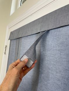 a person is holding up a piece of fabric to the side of a window curtain