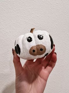 a hand holding a rock shaped like a cow's head with eyes and nose painted on it