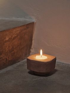 a lit candle sitting on top of a cement floor next to a wall and concrete block