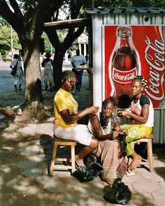 three women sitting in front of a coca cola sign