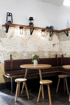 a table and benches in a room with lights on the wall above them, along with wooden stools