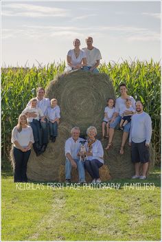 a group of people sitting on top of a hay bale in front of a corn field