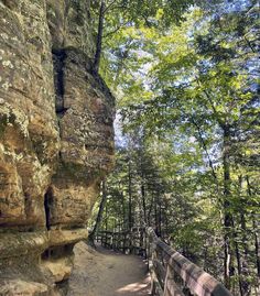 a wooden bench sitting next to a large rock face in the woods on a sunny day