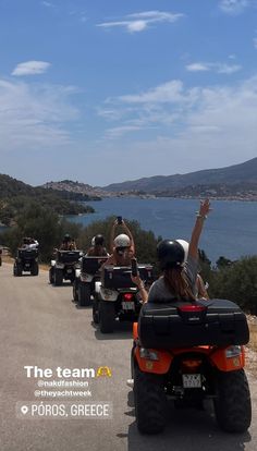 several people riding four wheelers on a road next to the ocean and hills with water in the background