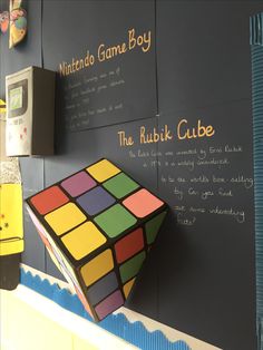 a rubik cube is hanging on the wall in front of a chalkboard with writing