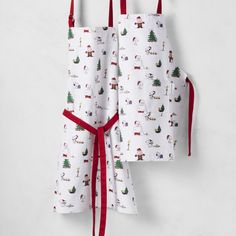 two aprons are hanging on the wall with red ribbon around them and one has santa's sleigh