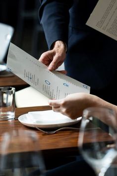 two people sitting at a table with plates and silverware in front of them, each holding a piece of paper