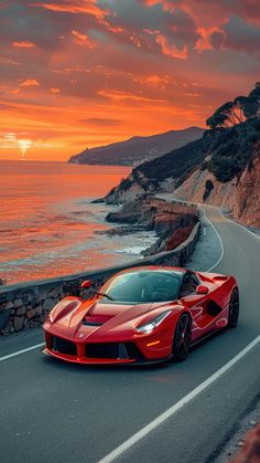 a red sports car driving down the road next to the ocean at sunset or sunrise