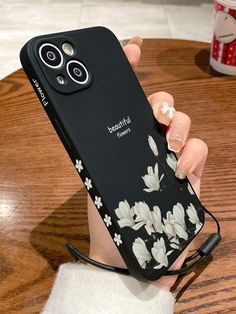 a woman holding up her phone case with flowers painted on the front and sides, while sitting at a table