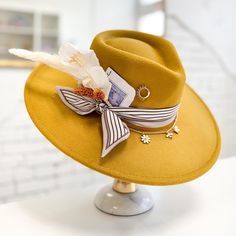 Golden Voyager is a Clover Lane Hat Bar original design. Mustard yellow felt hat. Neutral striped scarf and gold chain adorn the crown. A gorgeous dried floral bundle, burned art deco playing card, and simple sun pin brings it all together on the right side. The chain features three delicate charms hanging from it: a daisy, bee, and butterfly. Inner band is adjustable (fits most 54cm-59cm). Message me for a custom design! Terms & Conditions: Hats are not returnable. All sales final. Handmade Vintage Hat Bands For Spring, Gold Festival Hats For Spring, Bohemian Gold Hat For Kentucky Derby, Gold Bohemian Hat For Kentucky Derby, Vintage Felt Hat For Fall Festival, Bohemian Yellow Hat For Festival, Handmade Bohemian Felt Hat For Spring, Yellow Bohemian Fedora Hat, Yellow Bohemian Adjustable Hat