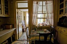 a dining room table and chairs in front of a window with curtains on the windowsill