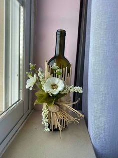 a vase with flowers in it sitting next to a wine bottle on a window sill