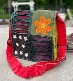 a small purse with an orange flower on it sitting on the ground next to a piece of wood