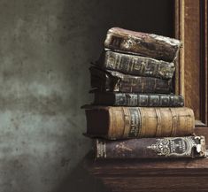 a stack of old books sitting on top of a wooden table next to a mirror