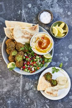 two plates filled with different types of food on top of a table next to dipping sauces and pita bread