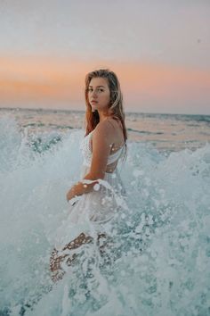 a woman is standing in the water at sunset