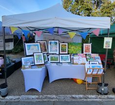 there are many pictures on the table under the tent and in front of it is an easel