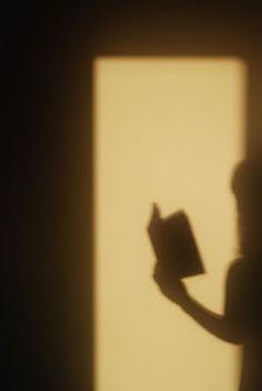 the shadow of a person holding a book in front of a window with light coming through it