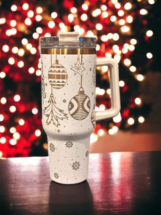 a white coffee cup sitting on top of a wooden table next to a christmas tree