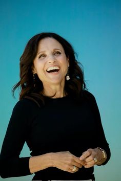 a smiling woman with her hands on her hips, wearing a black top and gold bracelets