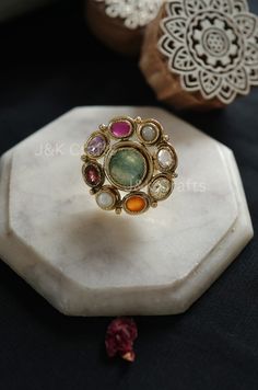 Skillfully made using classic methods, the ring features a fragile design embellished with semi-precious navrattan gemstones and the radiance of multicolored stones. These stones impart a touch of sophistication to this timeless treasure. Enhance your fashion with this exceptional ring. Closure - Adjustable Weight- 17gms Handcrafted in Jammu and Kashmir Paisley Pop travels the depths of India to learn techniques and crafts from deep down in the local markets and villages. We give utmost importance to our quality and packaging. Our goal is to ensure you receive exactly what you are looking for and for your experience to be special and memorable. We are ready to help and advise you through your purchase. IT' S  A W E S O M E * Our lovely packaging is designed by our co-founder Tanya. And all Luxury Elegant Meenakari Rings, Elegant Multicolor Ruby Ring, Fusion Style Multi-stone Round Jewelry, Multi-stone Round Fusion Jewelry, Fusion Style Round Multi-stone Jewelry, Elegant Multicolor Ruby Ring With Accent Stones, Elegant Multicolor Gemstones With Center Stone, Multicolor Gemstone Jewelry For Ceremonial Use, Elegant Multicolor Multi-stone Ruby Ring