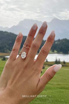 a person's hand with a diamond ring on top of their finger in front of a lake and mountains