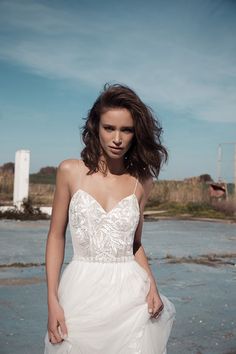 a woman in a white wedding dress standing on the beach with her hair blowing in the wind