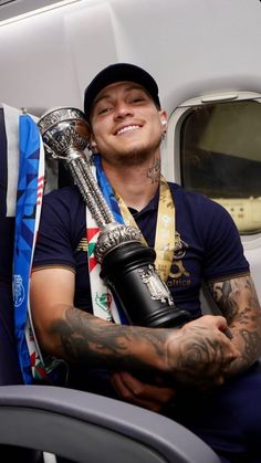 a man sitting on an airplane holding a trophy and wearing a baseball cap with his arm around him