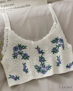 a white crocheted top with blue flowers on the bottom and green leaves on the side