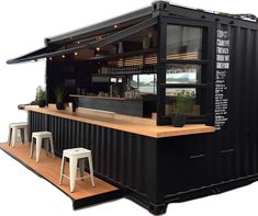 a black container bar with stools next to it on a wooden platform in front of a white wall