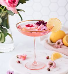 a pink drink with flowers and lemons in the background on a marble table top