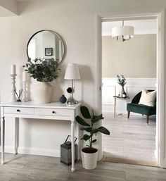 a living room with white furniture and a mirror on the wall next to a potted plant