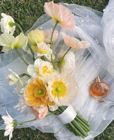 an arrangement of flowers on the ground next to a perfume bottle and some tulle