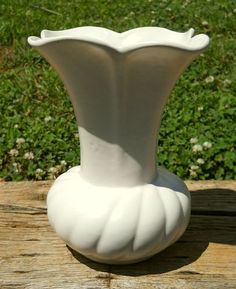 a white vase sitting on top of a wooden table in front of some green grass