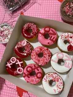 a box filled with lots of donuts on top of a pink and white table