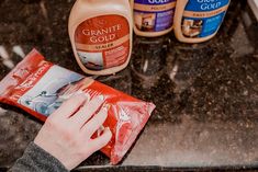 a person's hand on a bag of cleaner liquid next to other cleaning products