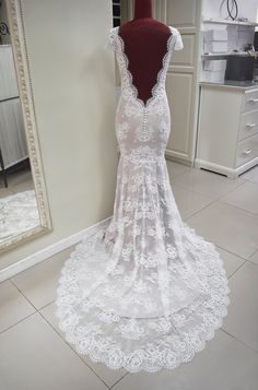 a white wedding dress on display in front of a mirror with a mannequin behind it