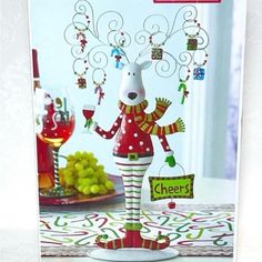 a christmas card with a reindeer holding a wine glass and some grapes on the table