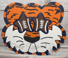 an orange and black tiger head with two footballs on it's face, in the shape of a heart