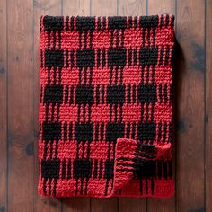 a red and black crocheted blanket sitting on top of a wooden floor next to a wall