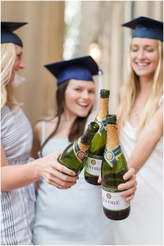 three women in graduation caps and gowns are holding two bottles of champagne while one woman smiles at the camera