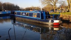 a blue and white boat floating on top of a river next to grass covered banks