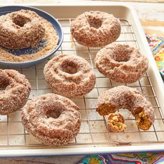 several donuts on a cooling rack next to a bowl of powdered sugar and a spoon