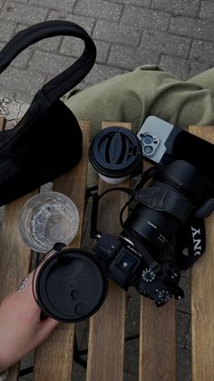 a person sitting on a wooden bench with a camera and coffee cup next to them