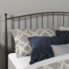 a bed with two pillows on it and a headboard made of metal, against a gray wall