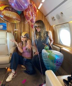 two women sitting on an airplane with balloons and streamers in the air behind them