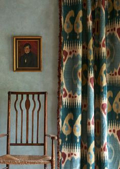 a chair sitting in front of a painting on the wall next to a window with curtains