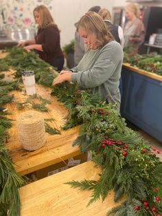 a woman is making christmas garlands at a table with other people in the background