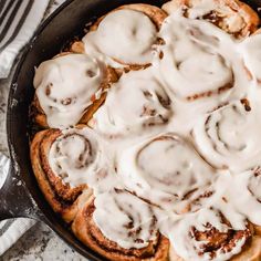 a pan filled with cinnamon rolls covered in white icing on top of a table