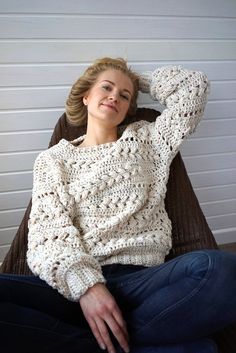 a woman sitting in a chair with her hand on her head and wearing a crocheted sweater